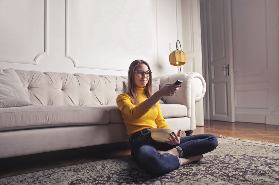 A woman relaxing in a bright living room with a television remote.