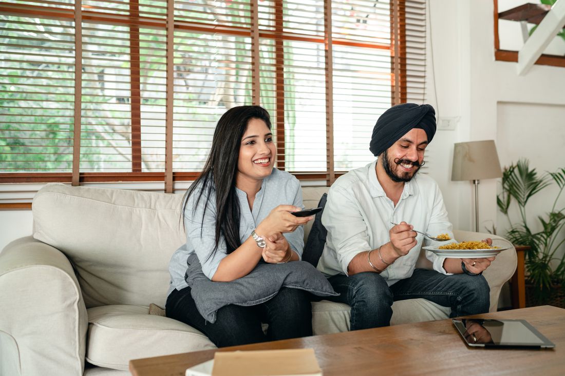 A couple sharing food while watching television at home.