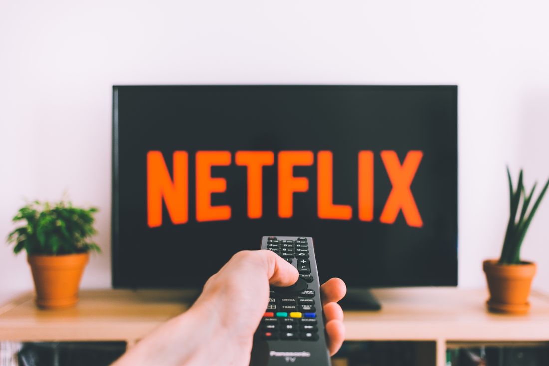A hand pointing a remote toward a television streaming screen.