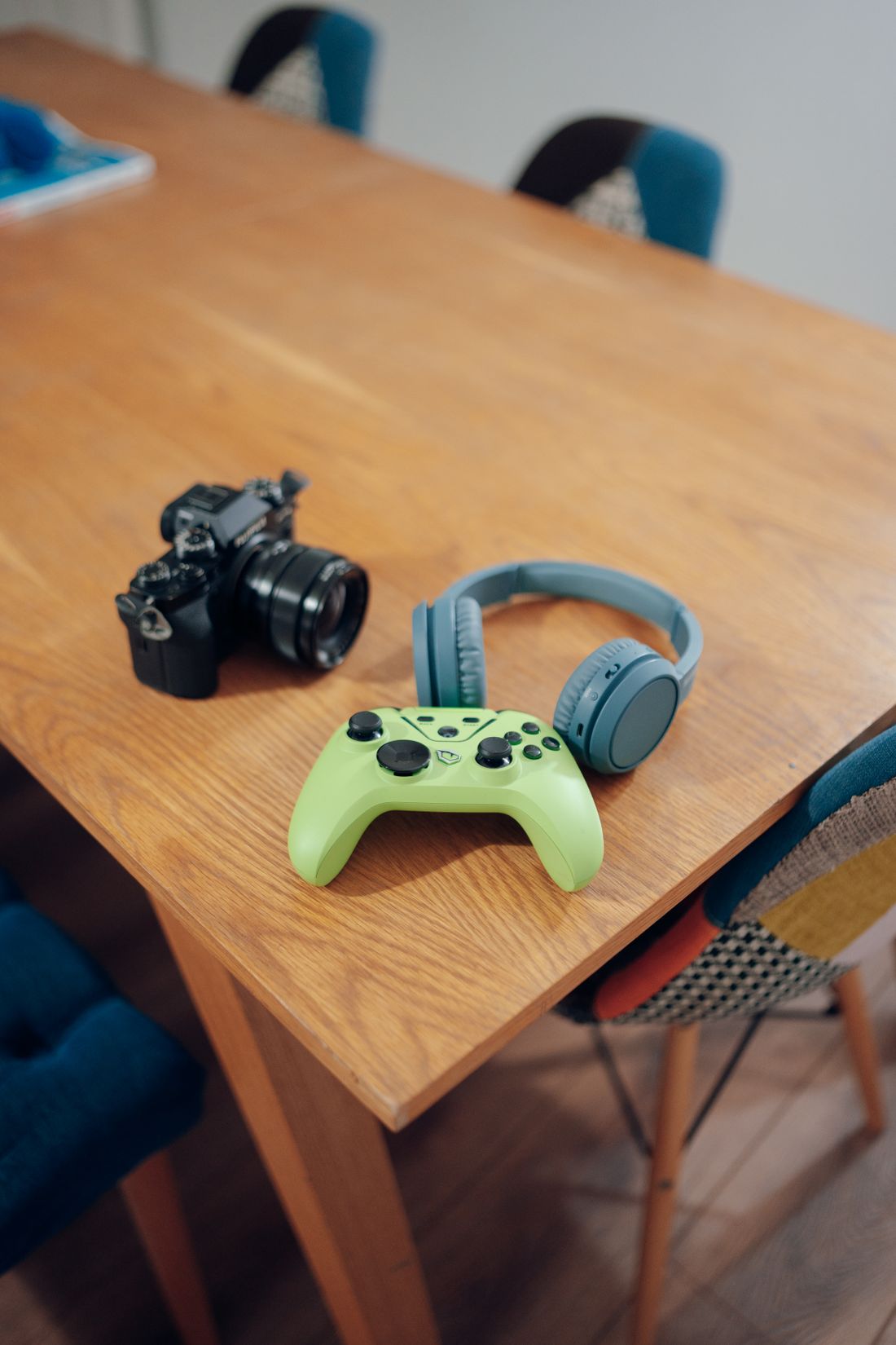 A camera, game controller and headphones on a wooden table.